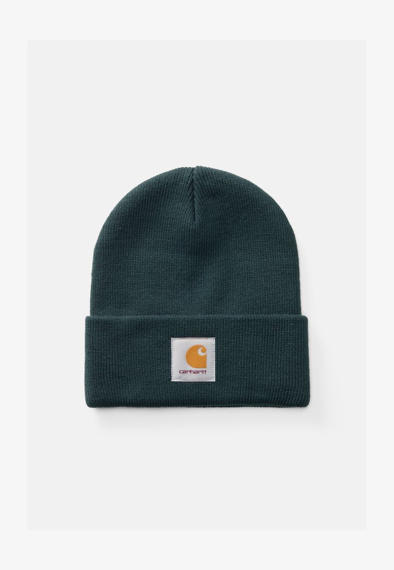 Mørkegrønn ribbestrikket lue med brettet oppkant som har en firkantet hvit lapp og oransje Carhartt-logo.
