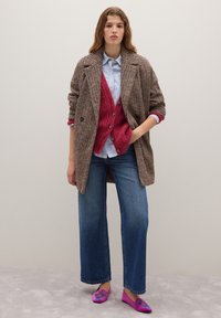 Blazer marrón de cuadros, cárdigan magenta, camisa azul a rayas, vaqueros de pierna ancha azul y bailarinas rosas bordadas, sobre un fondo neutro.