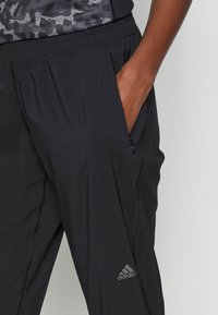 Svarta träningsbyxor gjorda av lätt, andningsbart tyg. Har ett elastiskt midjband, fickor på sidan och en liten Adidas-logotyp.