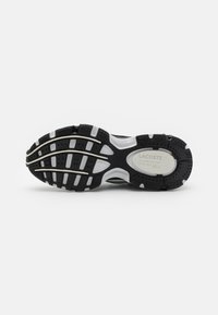 Czarno-biała podeszwa sportowego buta z wyraźnymi wzorami przyczepności, zaokrąglonym kształtem, gumowym materiałem i detalem w postaci logo Lacoste.