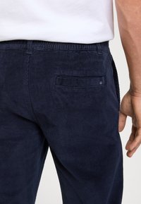 Granatowe spodnie z korduru z tylną kieszenią oraz fakturowaną, prążkowaną powierzchnią. Pas jest elastyczny dla komfortu i dobrego dopasowania.