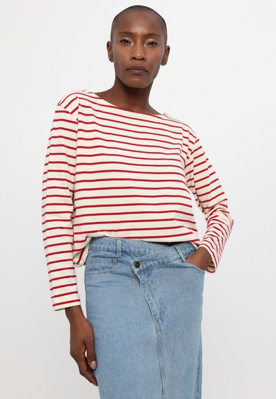 Rdeče in bele črtaste dolge rokave s čolnastim izrezom, v kombinaciji z svetlo modrim jeans krilom. Gladek material, sproščen kroj.