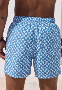 Bañador azul con estampado de huellas de manos blancas, cintura elástica y un bolsillo trasero, hecho de tela ligera que se seca rápidamente.