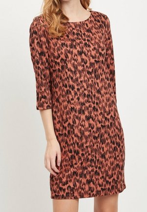 Woman wearing a knee-length, rust-colored dress with black abstract leopard print and three-quarter sleeves.