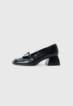 Scarpa nera in pelle con punta arrotondata e dettaglio a ritaglio. Presenta un tacco triangolare e un piccolo accento con fibbia.