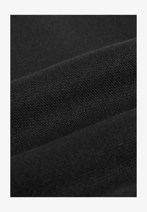 Nærbillede af sort stof med synlig strikket tekstur og bløde folder, der skaber blide kurver og skygger.