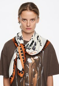 Siidist sall, millel on kreemjas alus, mustad lille- ja lehemustrid ning oranž äär. Seotud kaela ümber, pruun T-särgi peal.