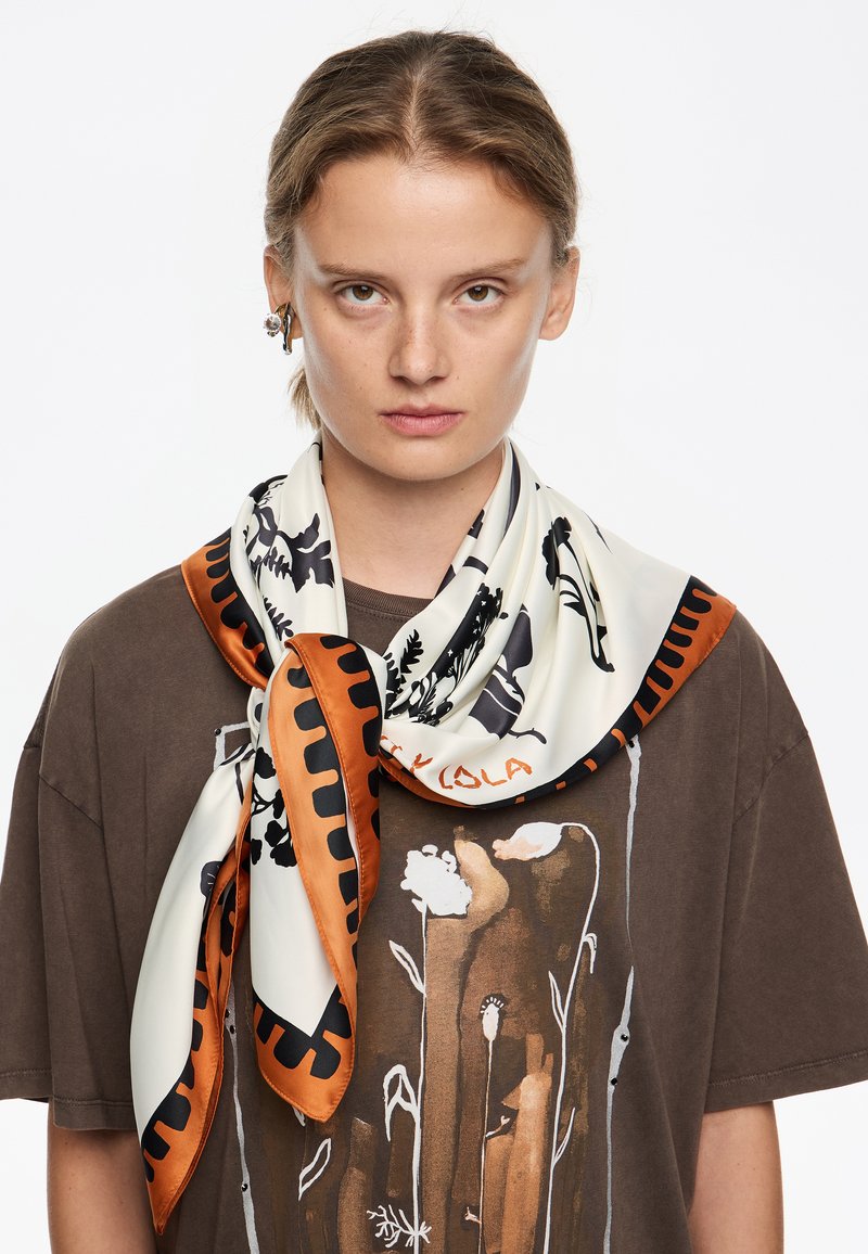 Siidist sall, millel on kreemjas alus, mustad lille- ja lehemustrid ning oranž äär. Seotud kaela ümber, pruun T-särgi peal.