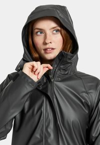 Svart vattentät jacka med huva, dragkedja fram och tryckknappar. Har en slät yta och justerbar krage för en säker passform.