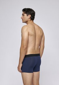 Mäns navy underkläder, tillverkade av ett stretchigt material, har en svart elastisk midja och en figurnära design, visad i profil.