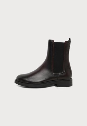 Botte Chelsea en cuir marron foncé avec panneau latéral élastique noir et talon bas empilé sur un fond clair.