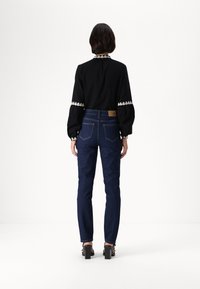 Μαύρη μπλούζα με μακριά μανίκια, λευκές λεπτομέρειες και φουσκωτά μανίκια, συνδυασμένη με σκούρα μπλε εφαρμοστά τζιν. Μοντέλο που φοράει μαύρες σανδάλια με τετράγωνο τακούνι.