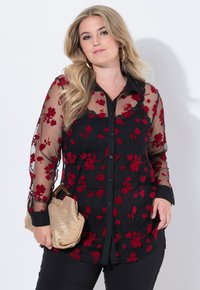 Chiuso con bottoni, blouse nera trasparente con ricami floreali rossi, maniche lunghe e colletto a contrasto nero. Abbinata a una borsa intrecciata dorata.