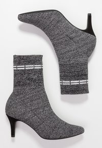 Bottes ankle en tricot gris avec une finition texturée, bout pointu et un talon de 3 pouces. Présente des accents de rayures blanches sur le revers.