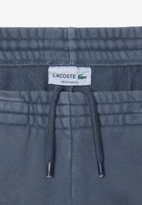Pantaloni sportivi grigi in cotone con vita elasticizzata, cordoncino e etichetta Lacoste con il logo del marchio. Design a vestibilità regolare.