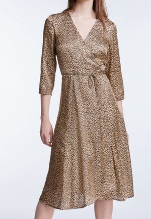 Frau trägt ein knielanges Wickelkleid mit Leopardenmuster, dreiviertel Ärmeln und V-Ausschnitt.