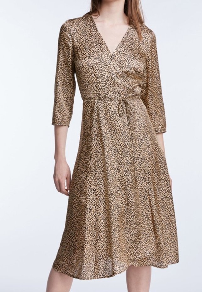 Femme portant une robe portefeuille à imprimé léopard longueur genou, avec des manches trois-quarts et un décolleté en V.