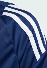 Närbild av marinblå tygaxel med tre parallella vita ränder på en sportjacka eller skjorta.