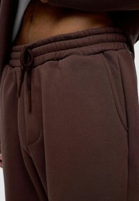 Donkere bruine sweatpants met een elastische tailleband en verstelkoord, voorzien van zijzakken en een gladde textuur.