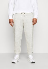Pantalones de chándal texturizados en gris claro con cintura ajustable y puños acanalados, combinados con una camiseta de manga larga blanca y zapatillas blancas.