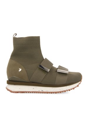 Zapatilla alta de color verde oliva con parte superior tipo calcetín acanalada, dos correas anchas con detalles metálicos, suela blanca salpicada y pastilla marrón.