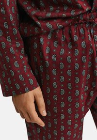 Hand resting beside maroon pants and shirt with blue and yellow paisley pattern and elastic waist detail.