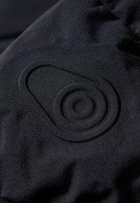La tela negra presenta un diseño circular y en espiral elevado, creando textura contra el fondo liso. El material parece suave y elástico.