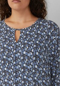 Bluse in Blau und Schwarz mit Muster, rundem Halsausschnitt und Schlüssellochdetail in der Mitte; leichtes Material, lockere Passform, dezente Textur.