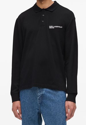 Czarna koszulka polo z długim rękawem, trzema guzikami i logo "KARL LAGERFELD JEANS", noszona z niebieskimi dżinsami.