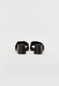 Black heeled sandals featuring a braided strap design, a sleek, rounded heel, and a textured finish on the upper material.