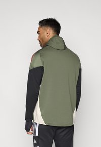 Κανένα τζάκετ με κουκούλα που διαθέτει έναν συνδυασμό ελαιόχρωμου, μαύρου και κρεμ χρώματος. Μαλακό ύφασμα με άνετη εφαρμογή και ανοίγματα για τον αντίχειρα στα μανίκια.