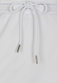 Pantalones cortos blancos con cierre de cordón y lazos anudados, acentuados por terminales plateados, hechos de una tela suave y ligera.