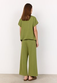 Green, loose-fitting top with short sleeves and wide-leg pants, both in a soft-textured fabric. Flat, brown footwear completes the outfit.