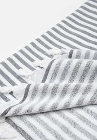 Tejido con franjas alternas de grosor grueso y delgado en gris y blanco. Bordes acabados con un suave fleco blanco. El material parece texturizado y tejido.