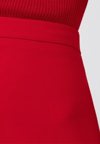 Röd kjol med en slät textur och strukturerad midjeband, med en figurnära design som smalnar av mot nederkanten.