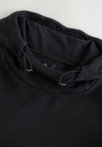 Tume-sinine kapuutsiga dressipluus, pehme ja tekstuurse kangaga. Kaeluses paelusega ning soonikkoes detailidega. Näidatud siseserva krae piirkond.