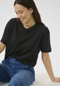 T-shirt in cotone nero con vestibilità rilassata, maniche corte e scollatura rotonda, abbinata a jeans in denim blu a vita alta.