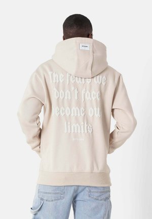 Beige hooded sweatshirt with white printed text on the back. Features ribbed cuffs and hem, soft texture, and a label at the neck.