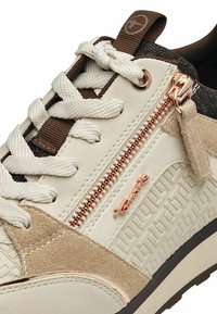 Bílé tenisky s texturovaným designem, béžovými semišovými detaily, zipem v růžovém zlatě a bílými tkaničkami. Na boku se nachází logo.