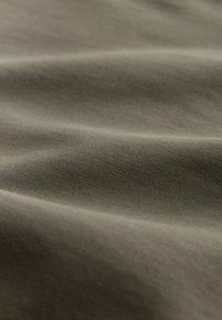 Gros plan sur un tissu doux de couleur vert olive montrant une texture de tissage fin et des plis délicats créant une surface lisse.