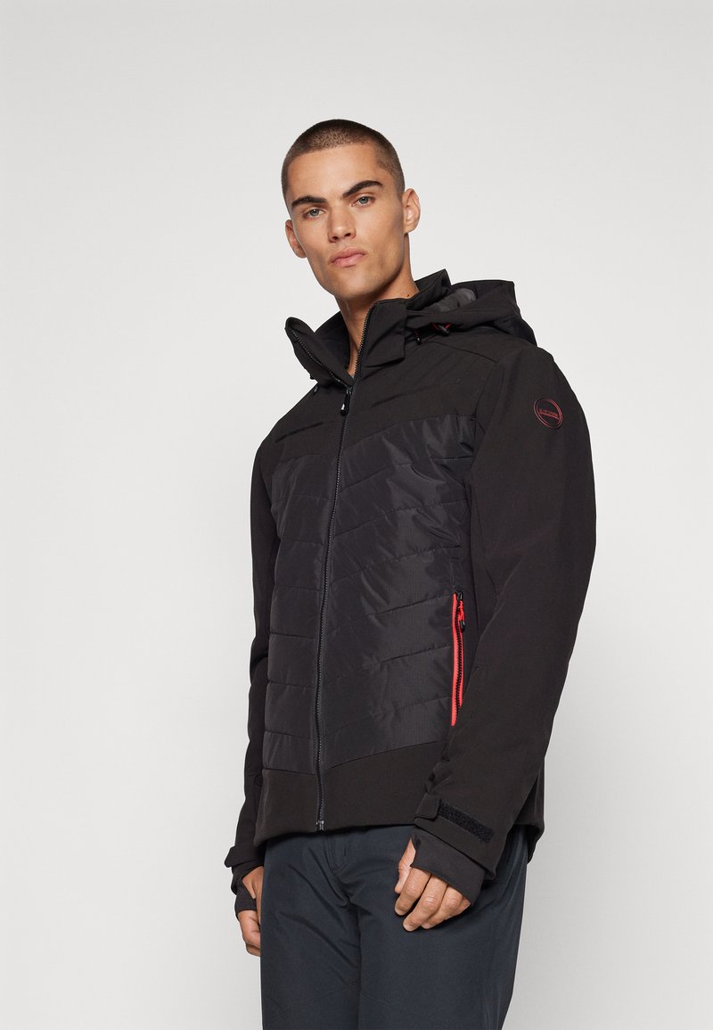 Schwarze Jacke mit gepolsterten Vorderpaneelen, Reißverschlusstaschen mit roten Akzenten, angesetzter Kapuze und Klettverschlüssen an den Ärmelabschlüssen; strukturierter Stoff.