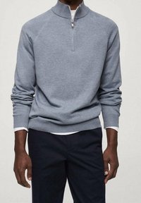 Grau melierter Baumwollpullover mit Viertel-Reißverschluss, Raglanärmeln, gerippten Bündchen und glatter Textur, kombiniert mit dunkler Hose.