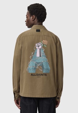 Homme portant une veste marron avec un grand "A" bleu enroulé de fils barbelés et un poing levé tenant une rose au dos, texte "ALLSAINTS" en dessous.