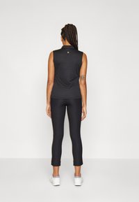 Top nero senza maniche con scollatura rotonda abbinato a leggings neri aderenti lungo la caviglia; entrambi realizzati in un tessuto liscio e elasticizzato.