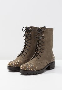 Olivově zelené semišové kotníkové boty s kulatou špičkou, zdobené dekorativním designem s cvočky na špičce a tradičním šněrováním.