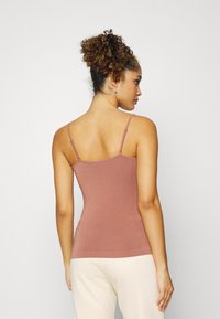 Camisola justa rosa claro com alças finas e uma textura suave. Apresenta uma bainha reta e um design minimalista. Adequada para camadas.