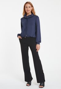 Navyfarbener Cowl-Neck-Oberteil mit langen Ärmeln und elastischem Saum, kombiniert mit schwarzen Schlaghosen mit Schlitzen an den Knöcheln. Glatte Textur, lässiges Design.