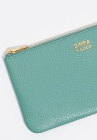 Mėlynos odos pouches su tekstūruotu paviršiumi, auksiniu užtrauktuku ir auksiniu logotipu, ant kurių parašyta "BIMBA Y LOLA".