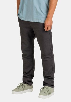 Dunkelgraue Hose aus einem strukturierten Stoff mit slim fit. Kombiniert mit hellgrünen Sneakers mit abgerundeter Spitze und Schnürsenkeln.