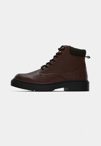 Braune Leder-Stiefelette mit schwarzer Gummisohle, runder Zehenpartie, Metallösen, schwarzen Schnürsenkeln und grünem Stoffkragendetail.